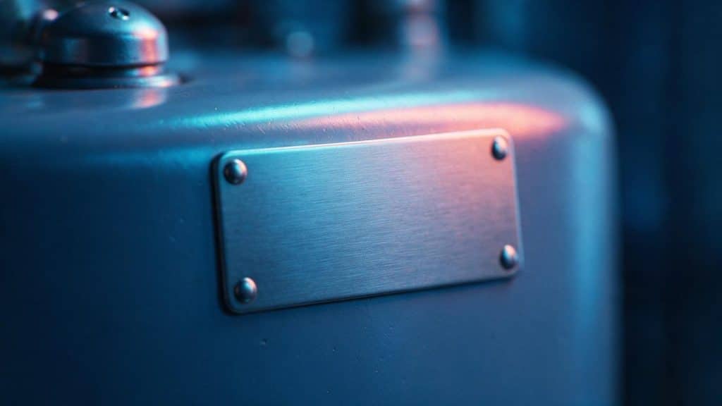 A close view of a blank, unstamped metal rating plate riveted to a water heater jacket